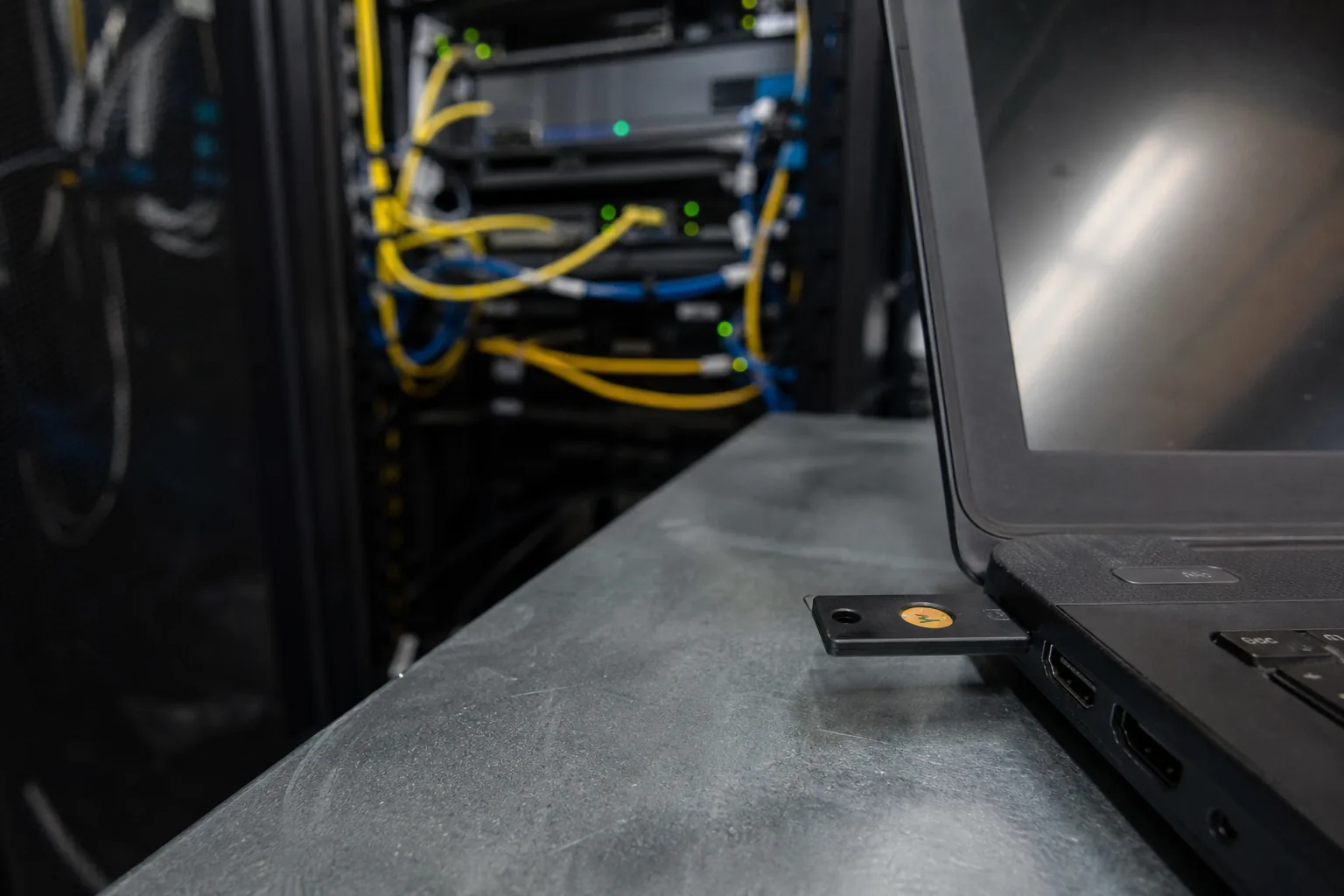 Hardware security key plugged into a laptop on a workbench in a police department server closet, with patch cables and a rack behind
