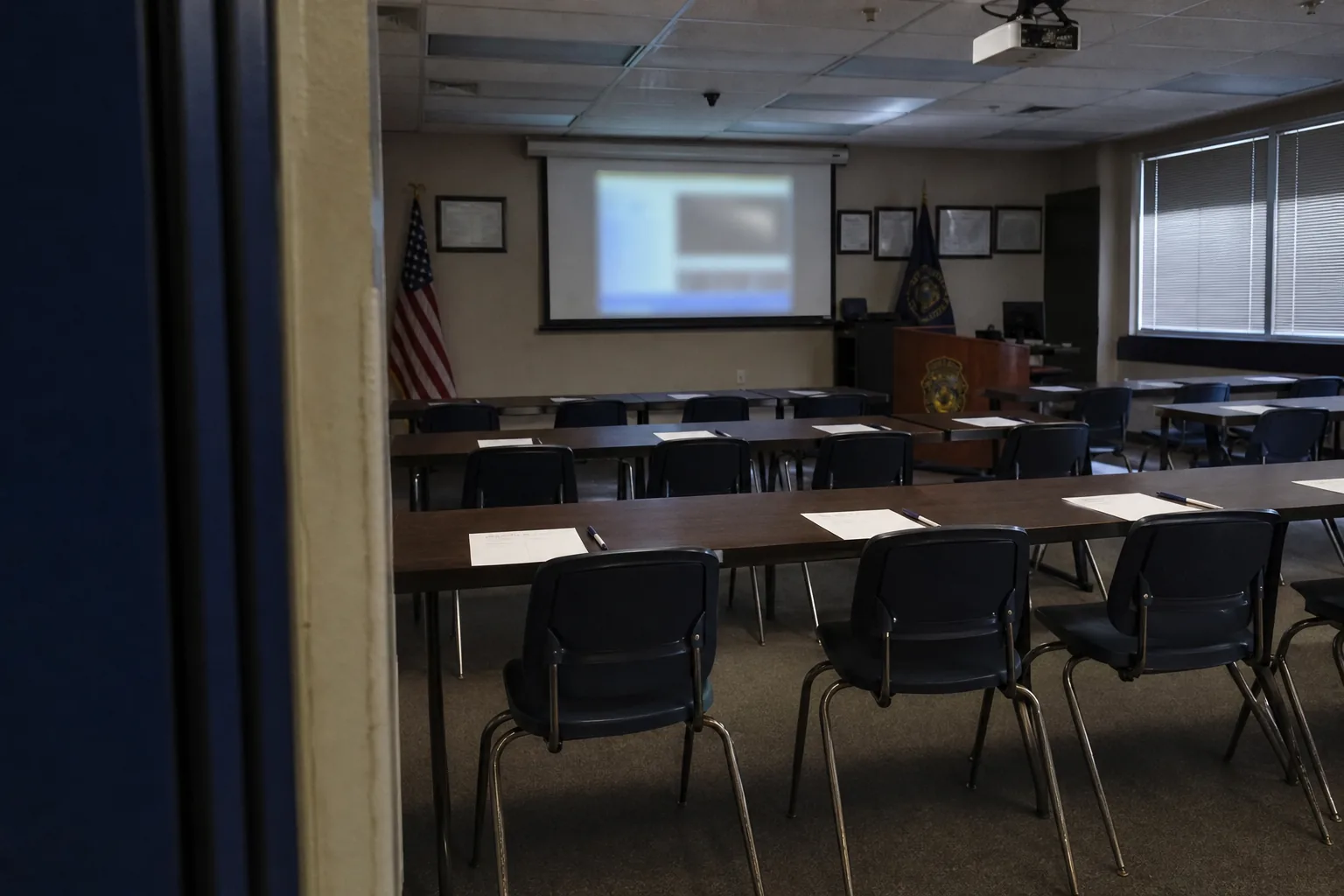 Empty police briefing room set up for security awareness training, with chairs facing a projector screen and printed handouts on the tables